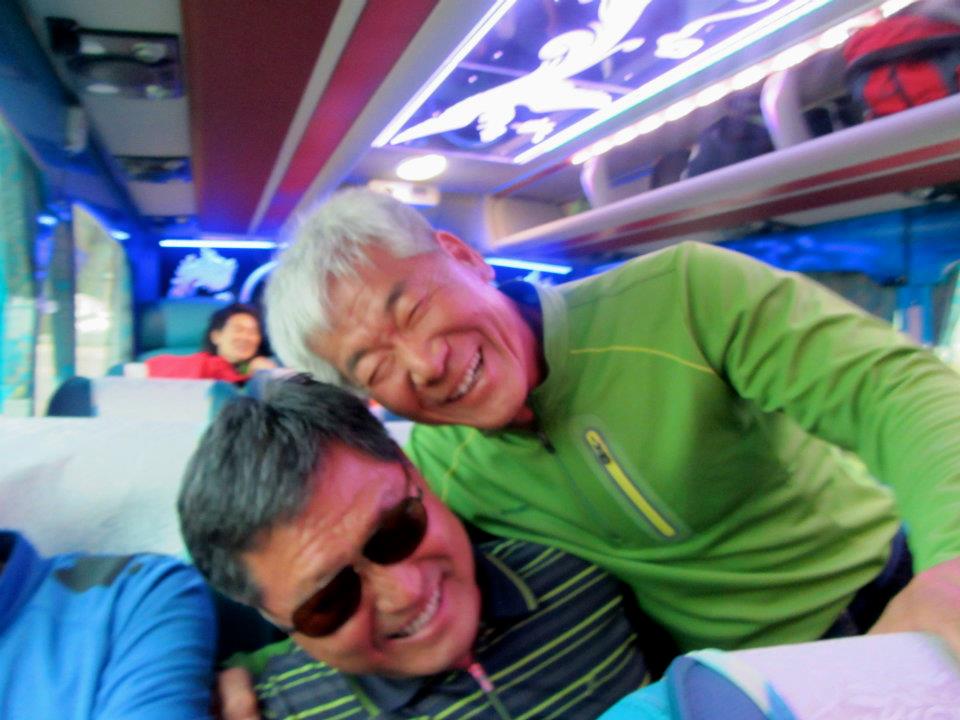 Older Korean men hugging and laughing on a karaoke bus to Samcheok.