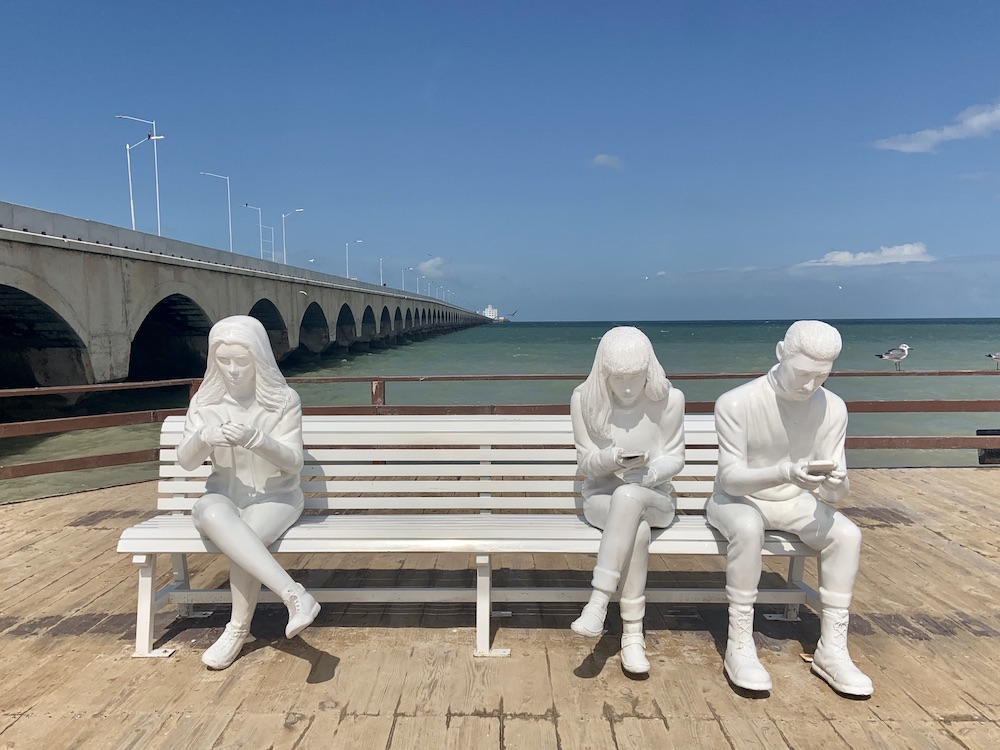 Sculpture of kids on a bench on their phones