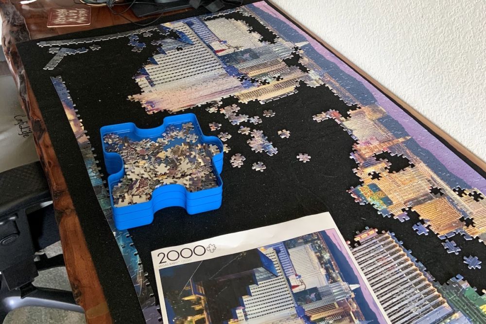 A black felt mat on top of a wooden desk with a partially completed 2000 piece puzzle of Las Vegas on it.