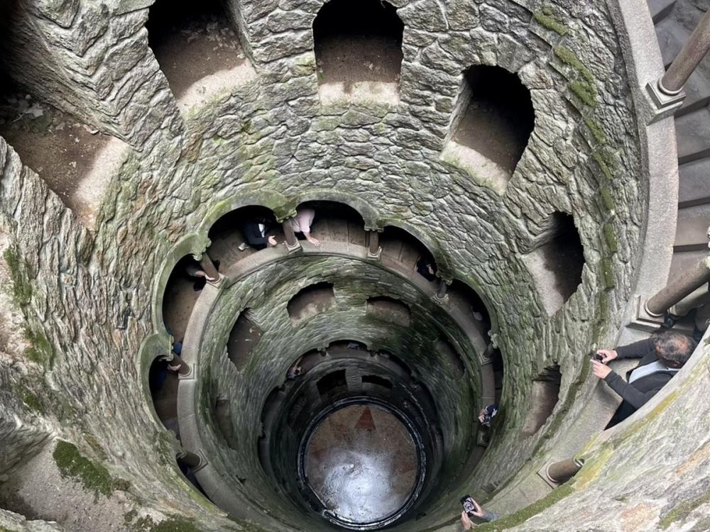 We peer down into a nine level well, the well of initiation in Sintra. A spiral stone staircase runs along the walls and we can see people descending the staircase.