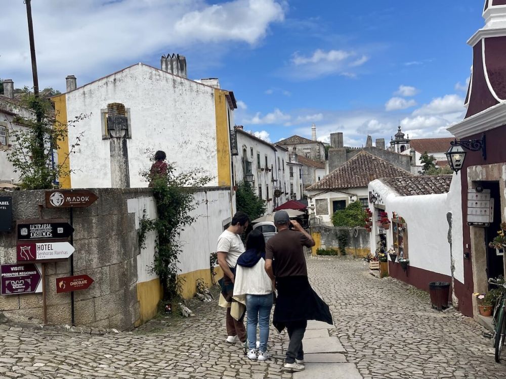 A group of three people seen from behind at the beginning of the main cobbled street in óbidos, portugal.