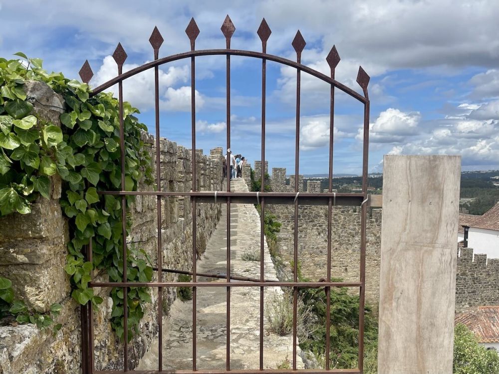 A rusty iron gate blocks passage along the ledge on the interior of the Óbidos city wall.