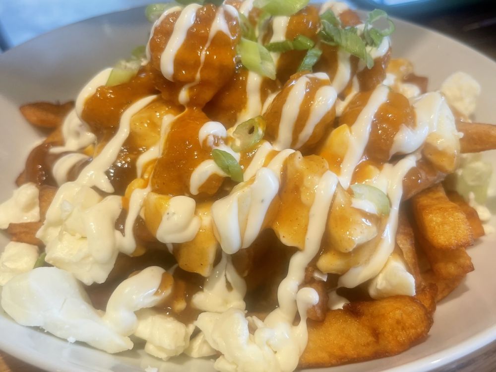 Buffalo poutine with green onions sprinkled on top and drizzled with ranch dressing. 