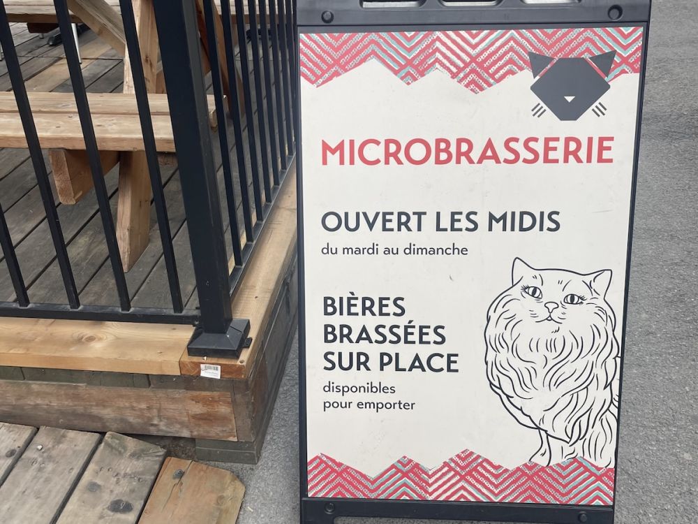 A-frame sign for a microbrasserie outside of a patio with a cat drawn on it