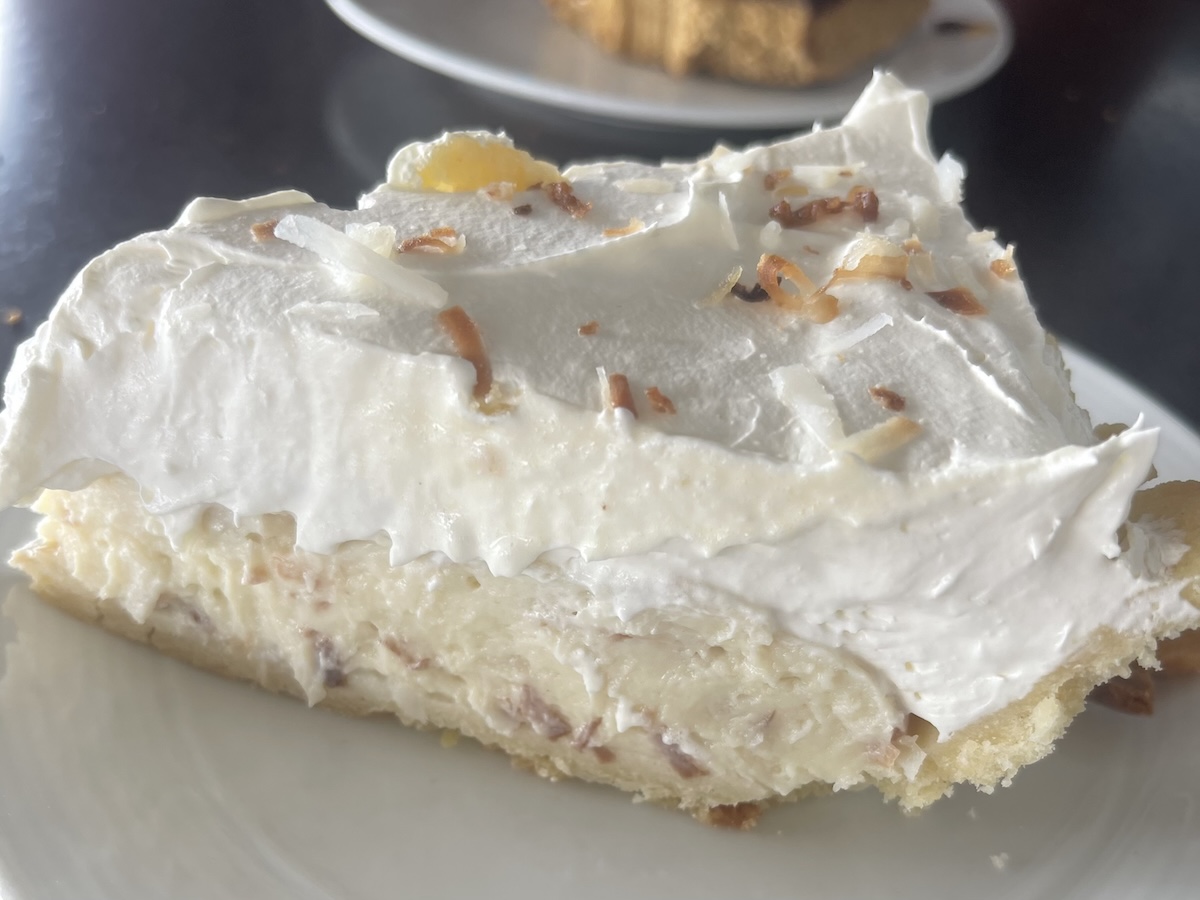 An extreme close up of a coconut cream pie, sprinkled with toasted coconut, on a white plate.