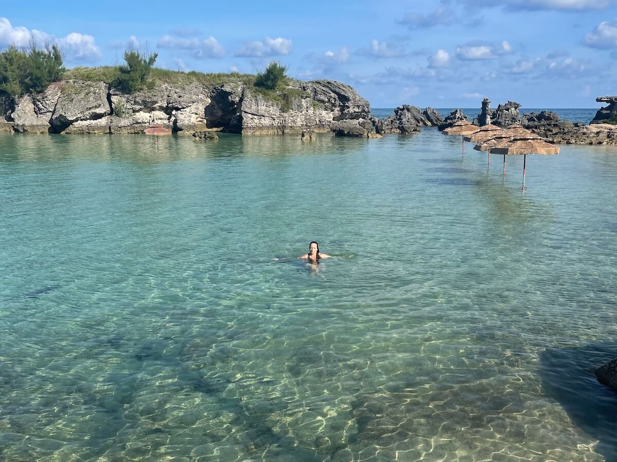 Lauren, a white woman, has all of Tobacco Bay to herself. It's a calm, sparkling body of water surrounded by rock formations, with several thatched umbrellas in the water.
